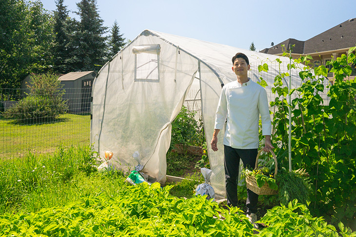 Chef Jun Young Park stands in front of his greenhouse overlooking his garden.