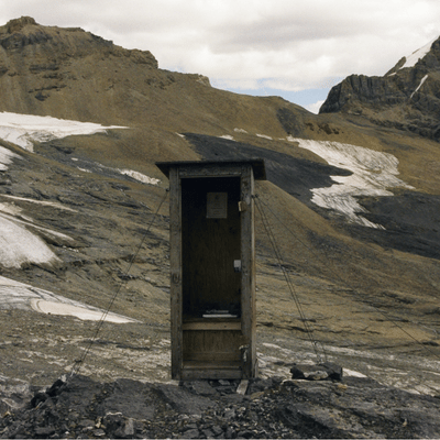 Outhouse in a rocky mountain landscape with patches of snow.