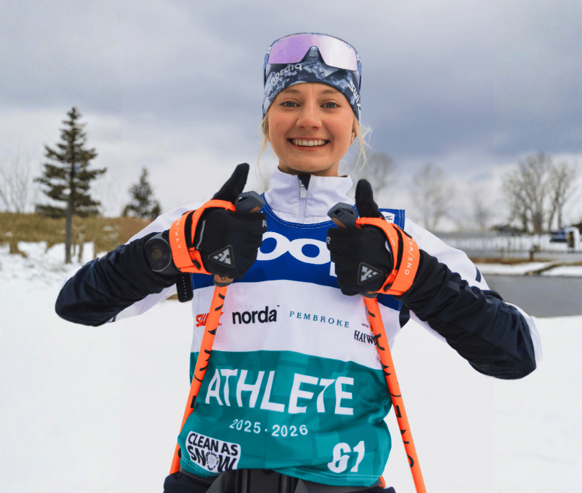 Young white woman in competitive ski gear with two thumbs up.