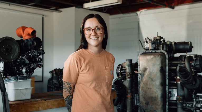 young woman wearing glasses and orange shirt standing in aircraft garage