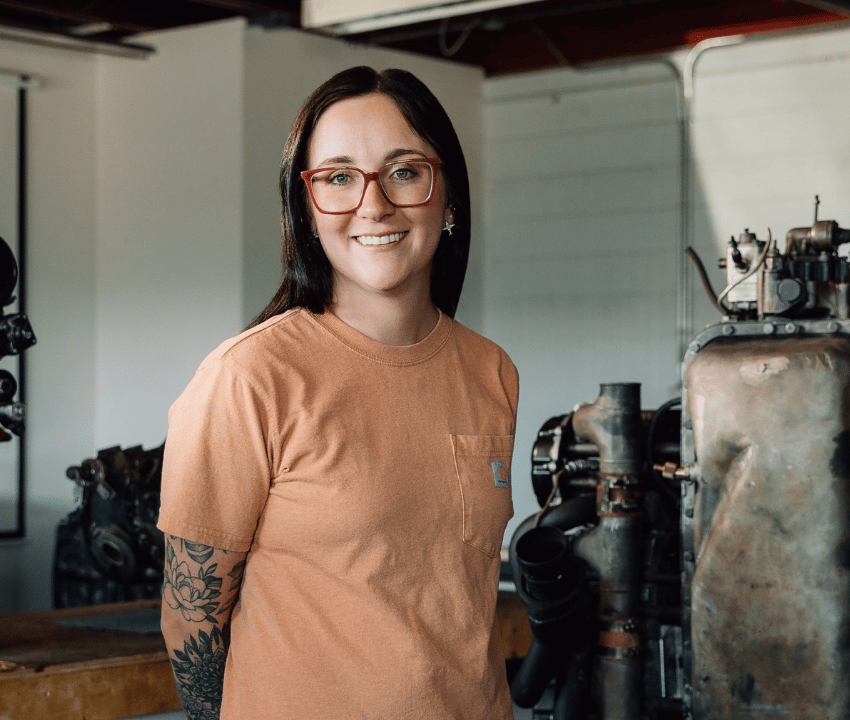 young woman wearing glasses and orange shirt standing in aircraft garage