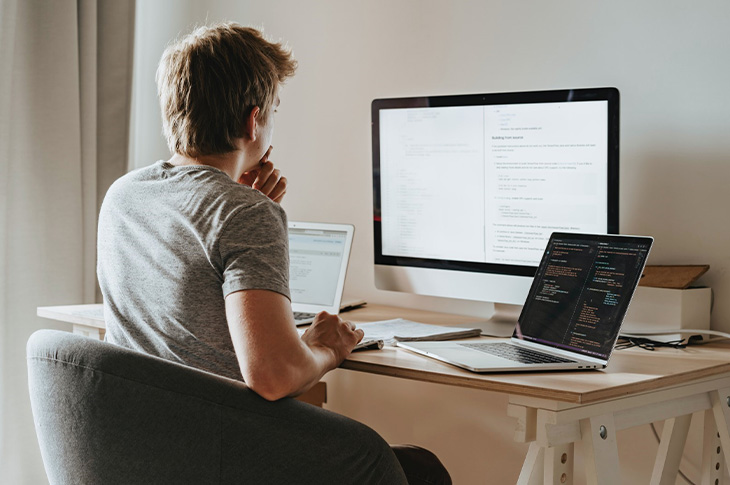 man looking at three monitors 