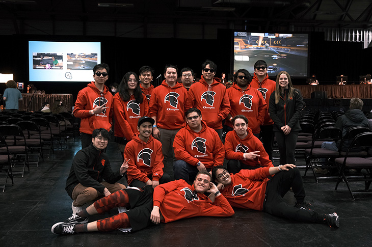 SAIT's esports team poses for a group picture with Rocket League gameplay being shown on projectors in the background.