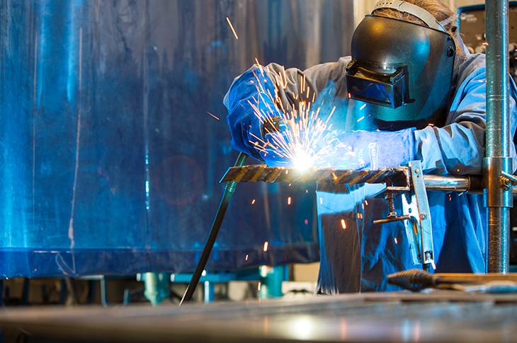 A student wearing a protective mask performs a weld with sparks flying
