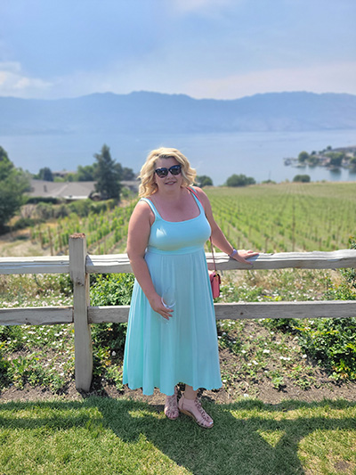 SAIT Information Systems Security alumna Lauren Schwering leans on a fence with a field, lake and mountains in the background