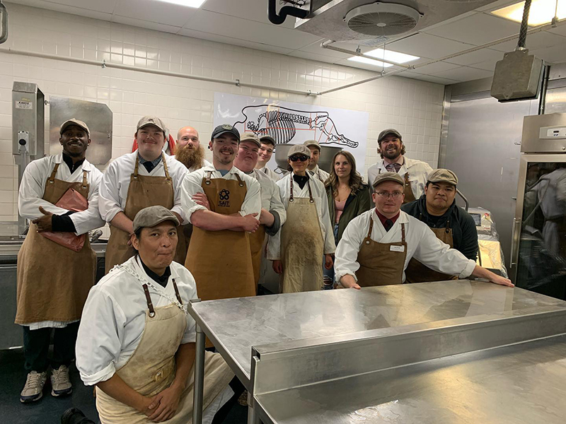 A group of butchery students smile in the butchery classroom at SAIT