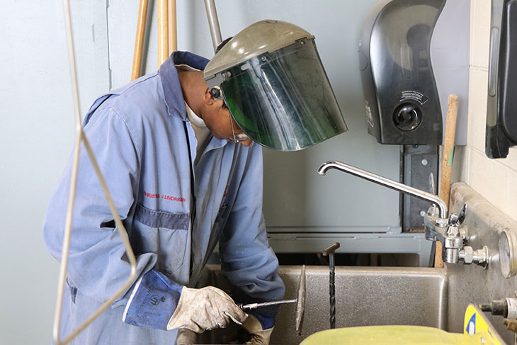 A student in lab coat with a welding mask lifted up.