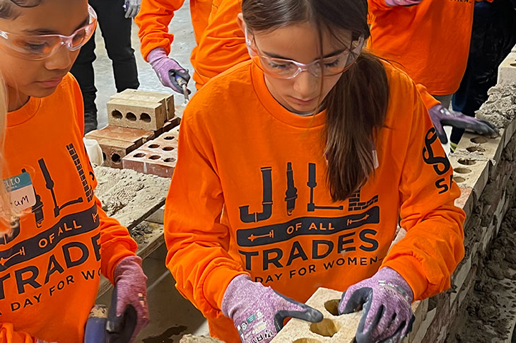girl in orange shirt putting mud on a brick to build a wall