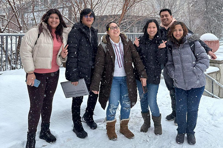 Students standing outside on SAIT's campus smiling while snow falls.