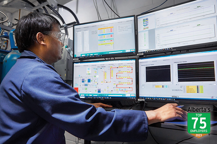 Person wearing safety goggles standing in front of four computer monitors 