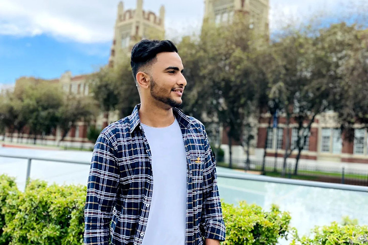 An individual stands on SAIT's main campus with trees and Heritage Hall in the background