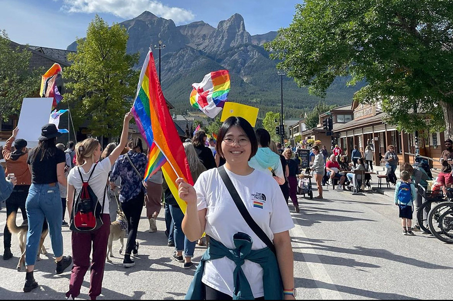 Haejin Han waves a pride flag while smiling with the mountains in the background