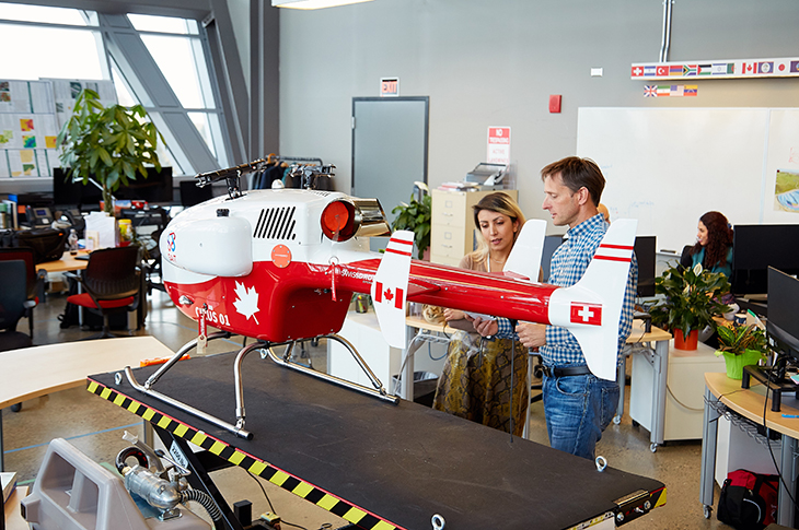 Two researchers investigate a large drone that is on a platform in the ARIS office at SAIT.