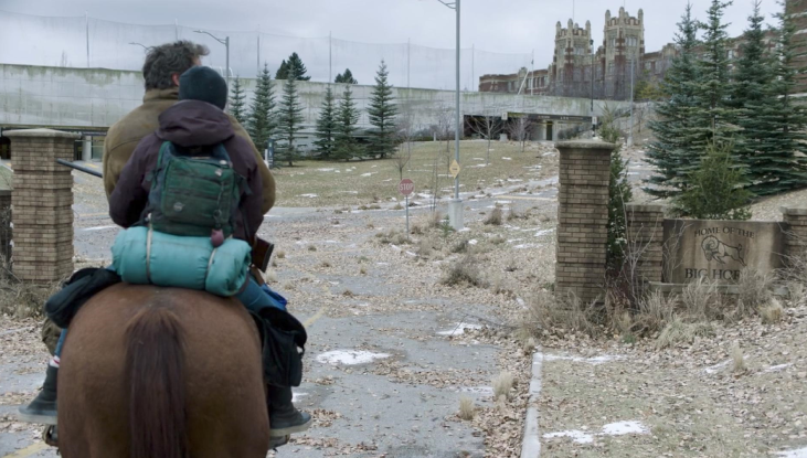 A view from behind Joel and Ellie as they ride a horse up to a university campus (featured in The Last of Us). The campus is actually SAIT.