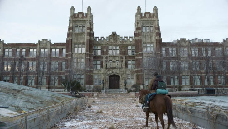 A view from behind Joel and Ellie as they ride a horse through a university campus (featured in The Last of Us). The campus is actually SAIT and SAIT’s iconic brick building, Heritage Hall, is featured front and centre.