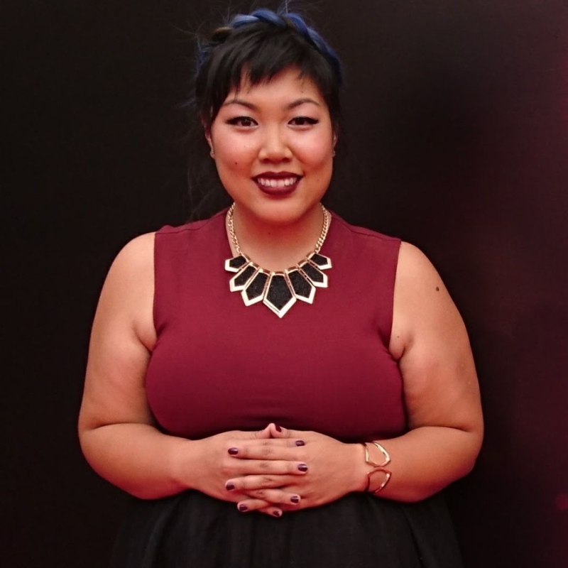 Headshot of Sound Assistant Val Siu, also a SAIT grad. Sue is wearing a red top, black necklace and has hands folded in front.