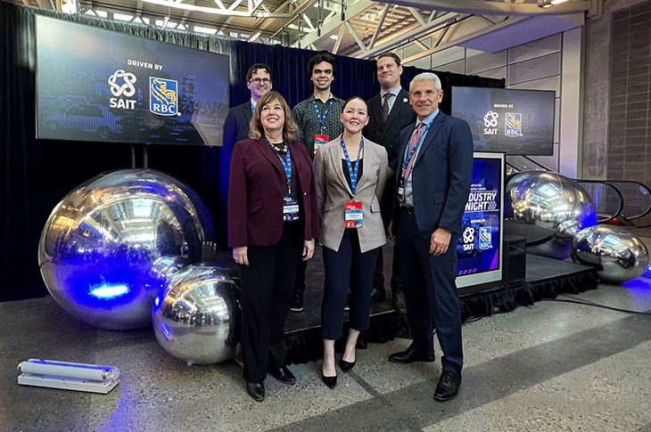 Representatives from SAIT and RBC stand on stage at the RBC announcement in Aldred Centre with SAIT and RBC logos displayed on screens in the background.