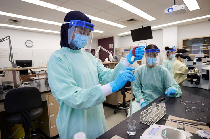 A student in medical protective gear, including a gown, face mask, face shield and gloves uses a pipette in a lab classroom.