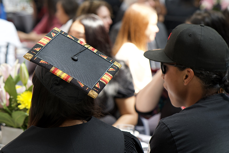 Someone in a decorated graduation cap sits at a table with others during the meal hour