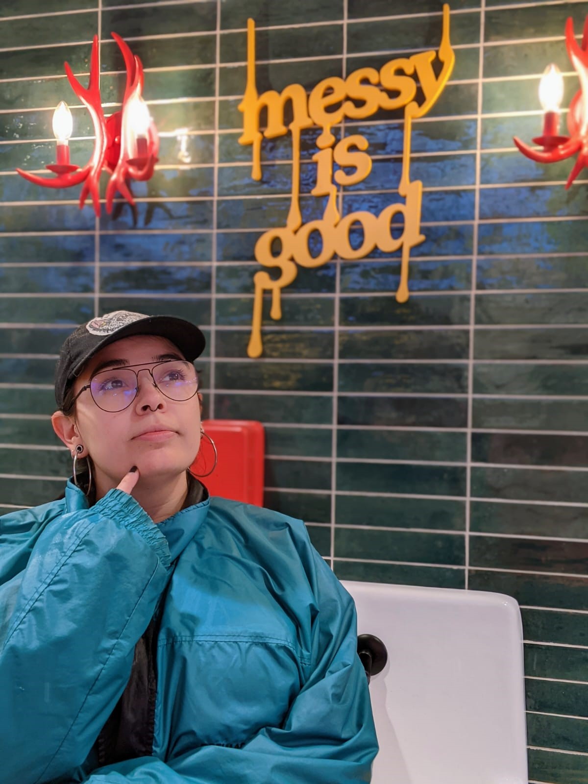 Amanda poses in a blue jacket and ball cap with a sign behind her that reads "messy is good."