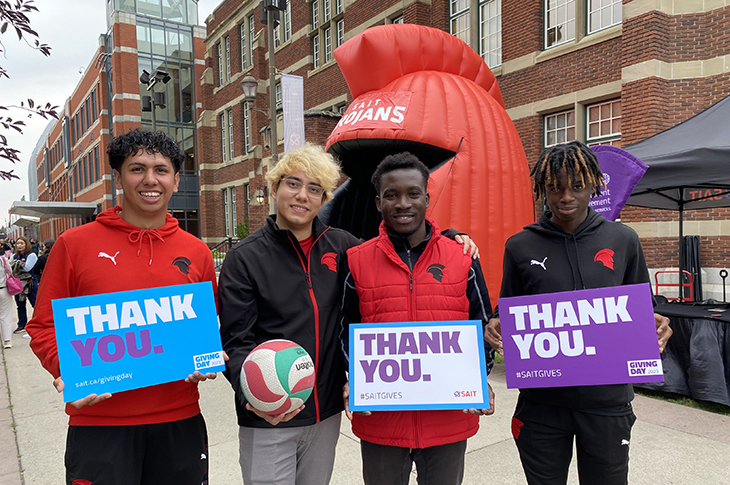 four sait students smiling outside Heritage Hall with thank you signs