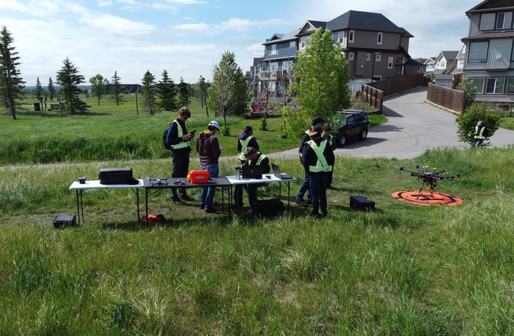 Six researchers stand at a folding table next to a drone on a portable orange helipad. 