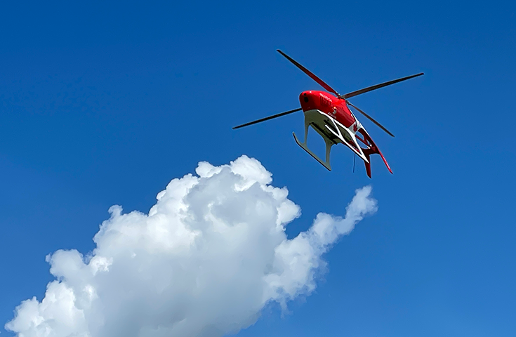 A helicopter drone flies in a blue sky with a white cloud in the background.  