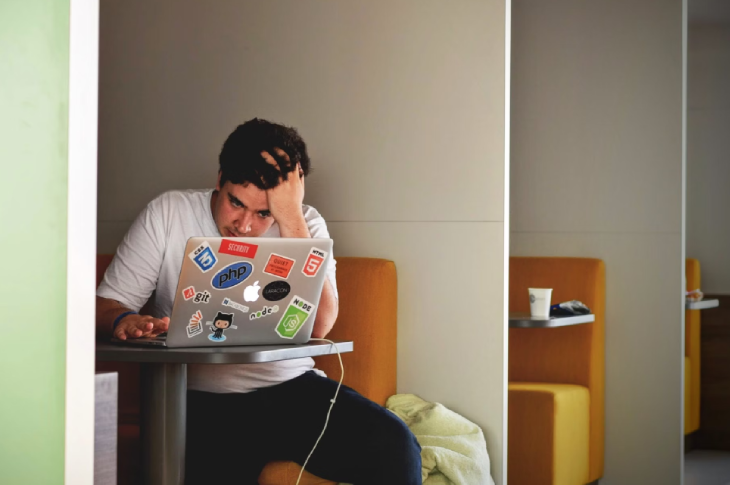 A student sits at a table looking at their laptop screen.