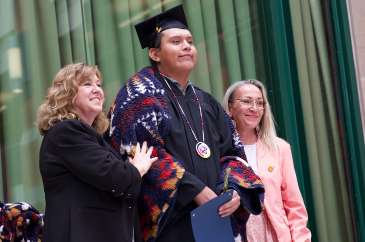 Heather Magotiaux, Vice President, External Relations, and Jennifer Russell participate in a Blanket Ceremony with a graduand at SAIT’s Spring 2023 Indigenous graduation celebration.