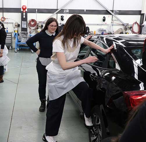 female staff member leaning up against a black car with her foot on a lug wrench