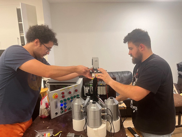 Two SAIT students stand at a table. Both are wearing black tee shirts. They are holding wires above a diorama of three grain bins.