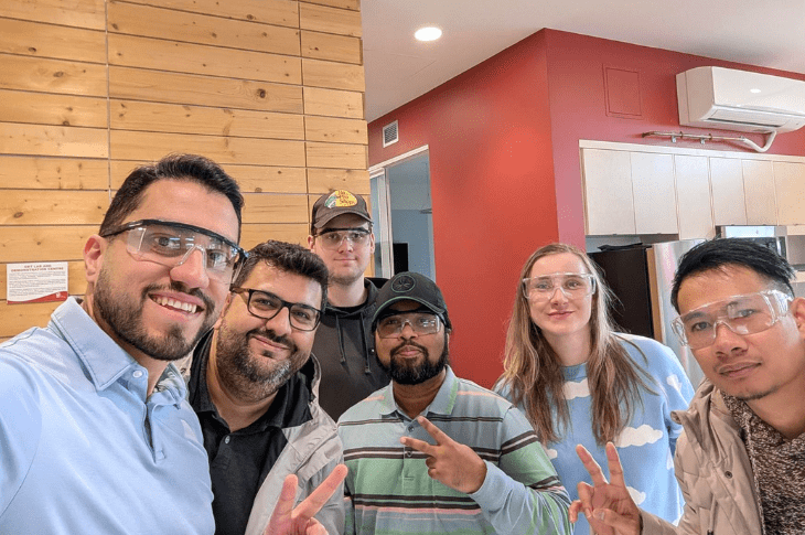 Six SAIT students smile at the camera, flashing peace signs. They are all wearing clear personal protective goggles.