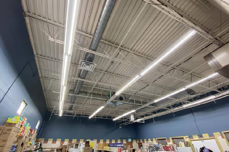Wide angle shot of a room with navy blue walls and a high industrial ceiliing made of corrugated white metal with three long white fluorescent lights lighting the space
