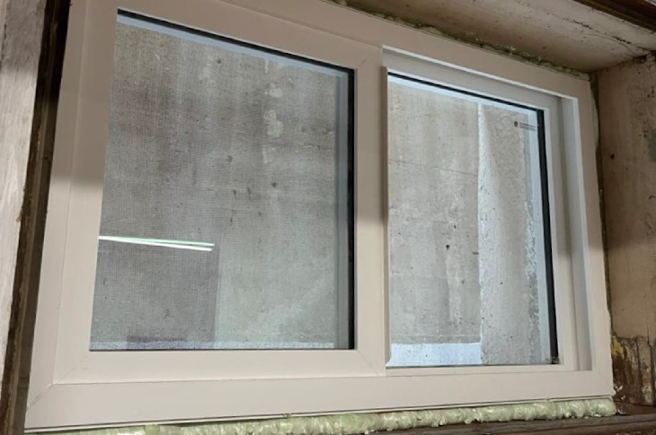A window, roughly one foot tall and two feet wide, with new insulation visible on the upper and lower edges.