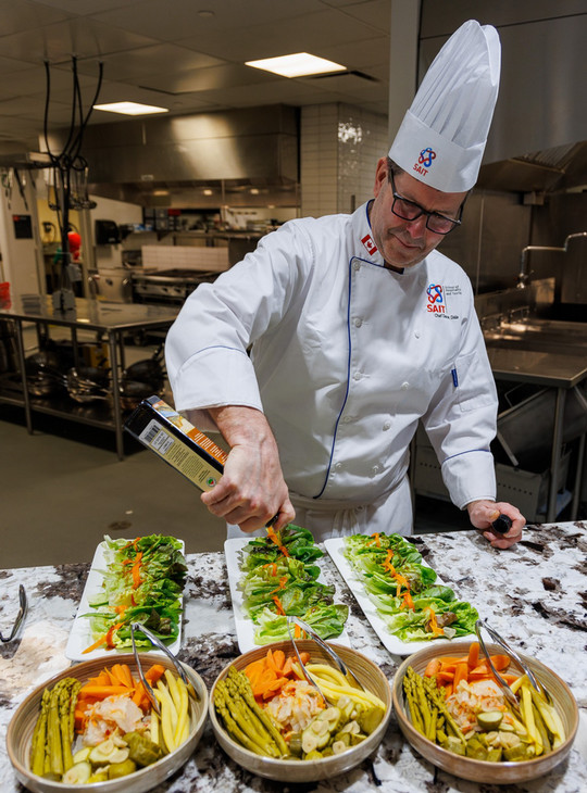Chef Derek Dale preparing multiple dishes in SAIT chef whites