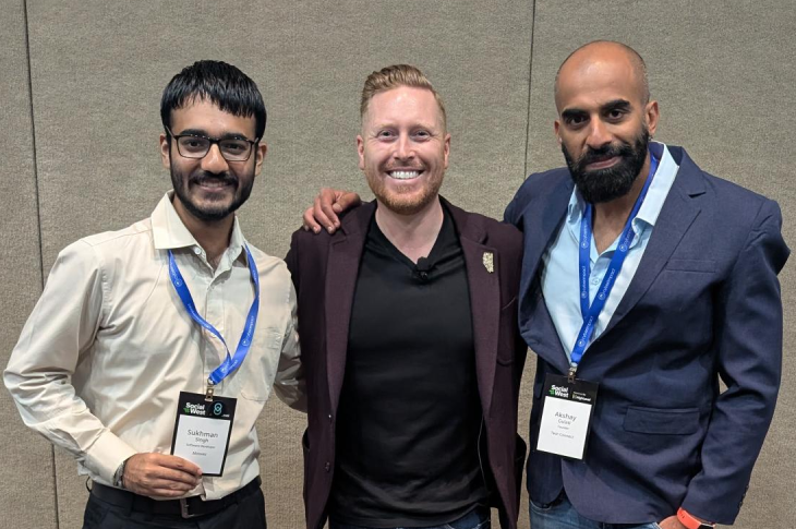 Sukhman stands with Ian Macdonald and Akshay Gulati in front of a neutral-coloured wall, all wearing suit jackets, name tags and smiling.