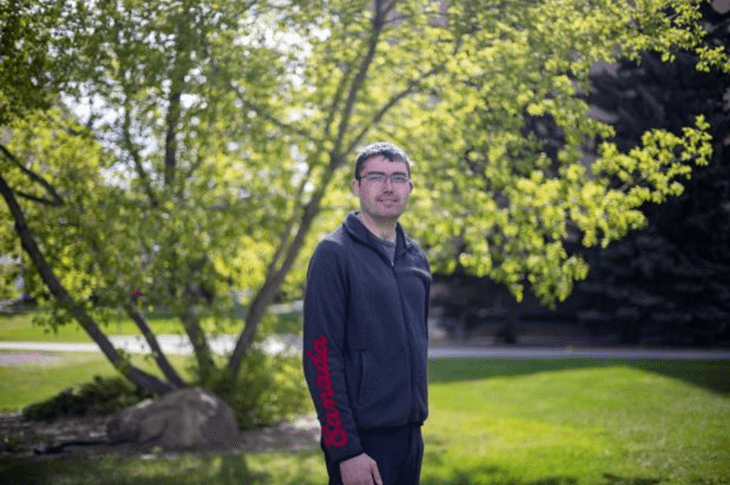 Austin Janz stands outdoors in front of a leafy tree, wearing a dark hoodie with "Canada" printed on the sleeve.