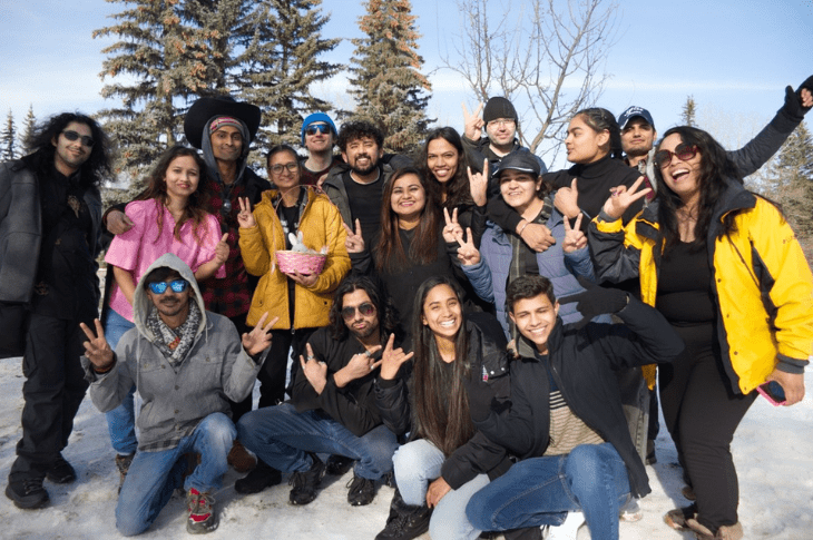 Group of friends posing cheerfully in a snowy landscape, making peace signs and smiling at the camera.