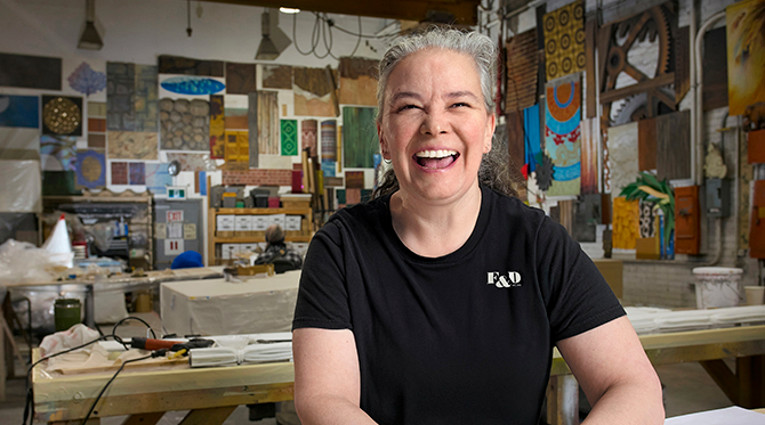 Shannon Fraser reviews plans in a theatre workshop with props on display in the background.