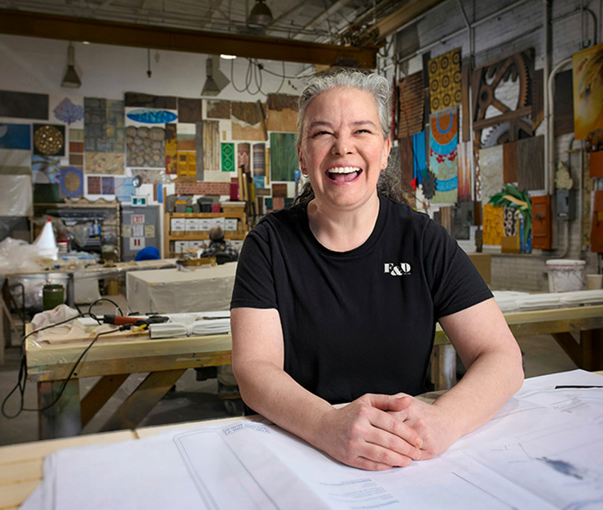 Shannon Fraser reviews plans in a theatre workshop with props on display in the background.