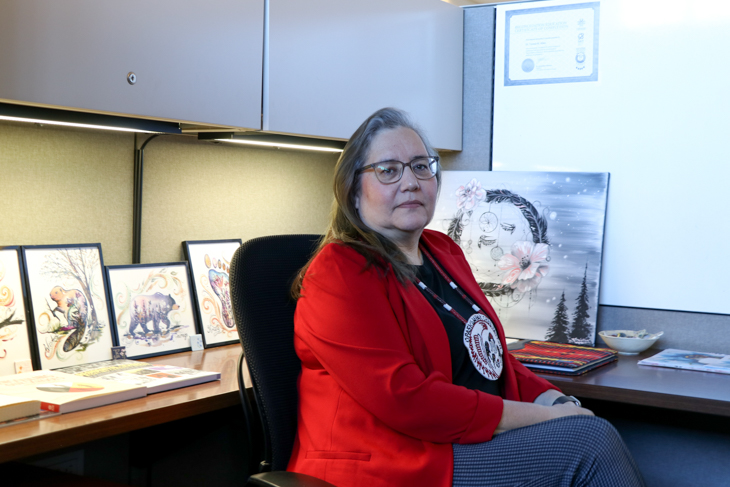Teresa Miles sits at her desk surrounded by Indigenous art