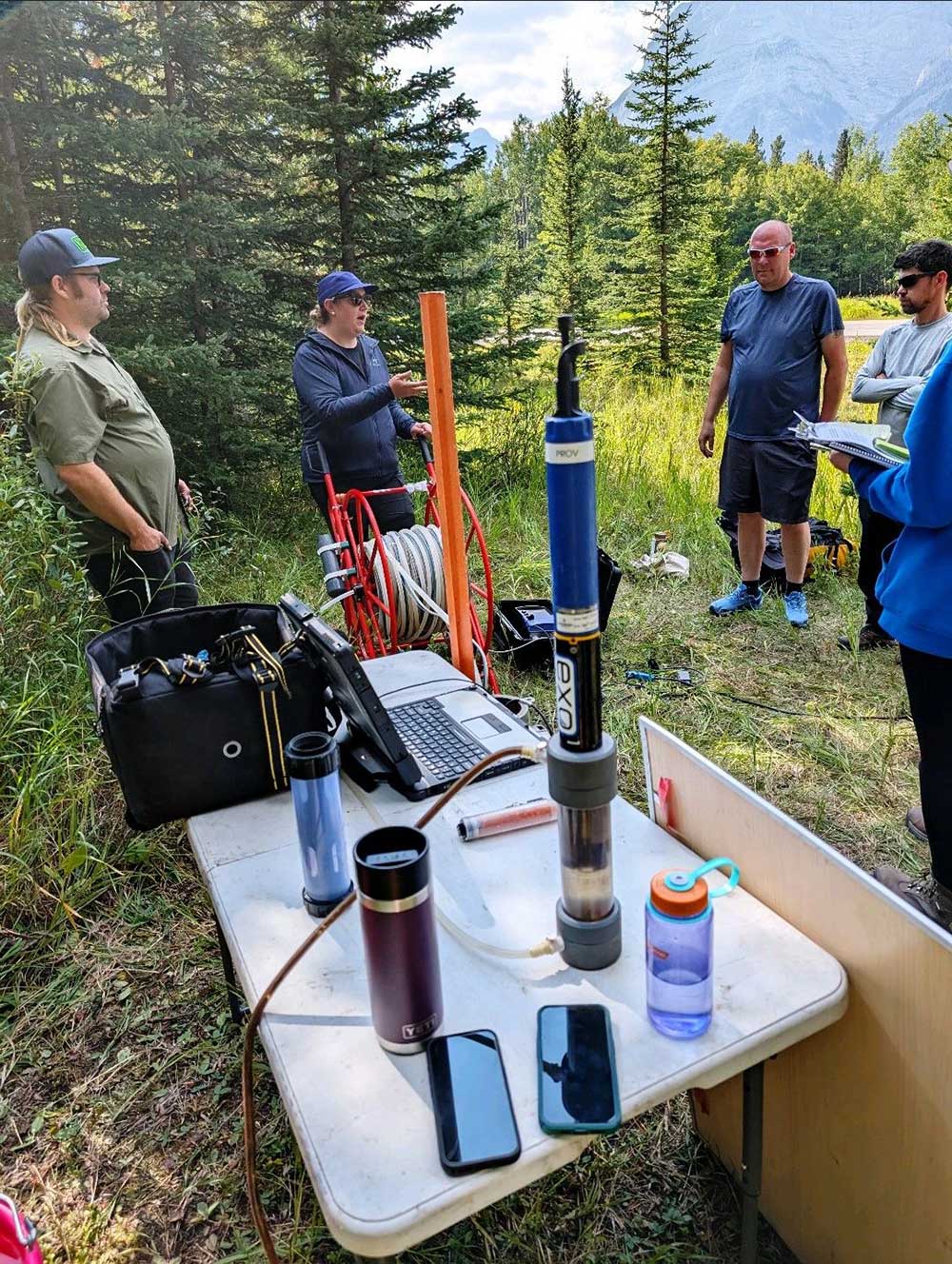 A group of people standing around a table with a computer and other objects