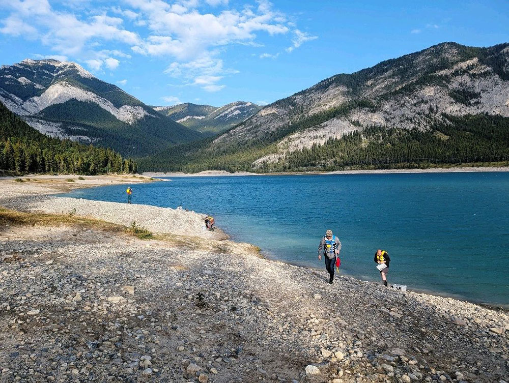 A group of people walking on a rocky shore by a lake