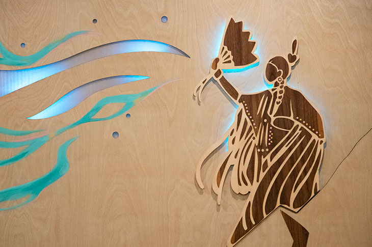 Natoysopoyiis mural made from engraved wood panels featuring pictographs from Blackfoot stories lit by LEDs