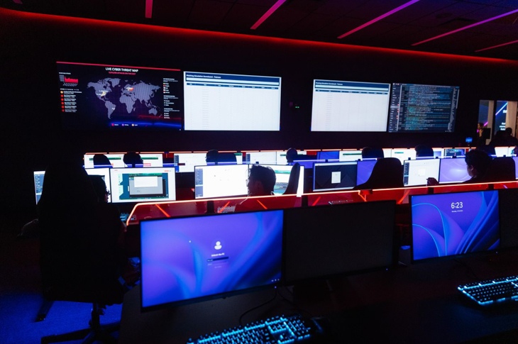 Central Command Centre with multiple computer screens displaying data and a world map, indicative of cybersecurity operations.