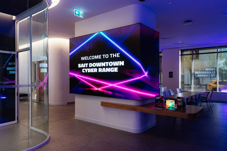 Signage displaying "Welcome to the SAIT Downtown Cyber Range" with vibrant neon lights in a modern interior space.