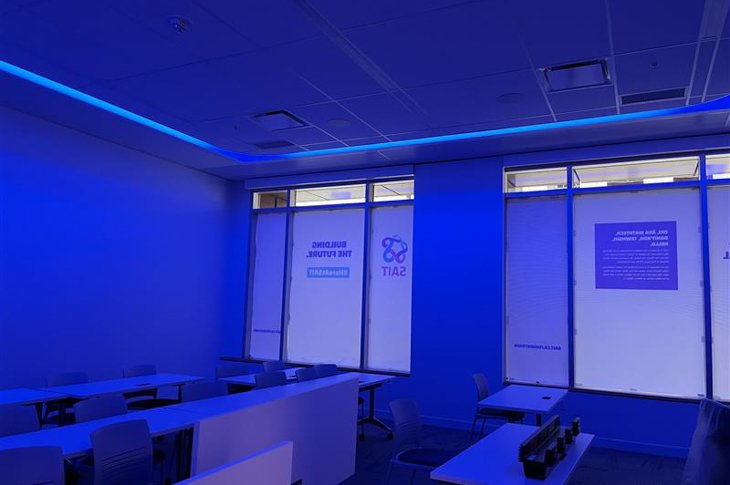 A classroom with blue ambient lighting and large windows displaying the SAIT logo.