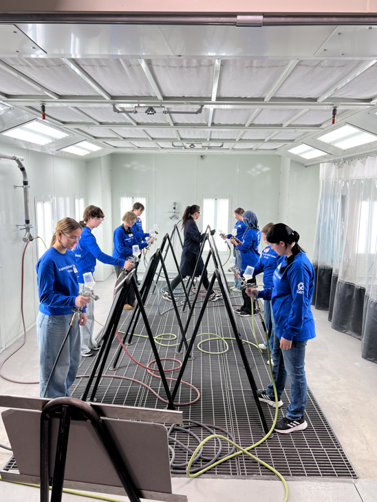 Students in a training room practice using spray equipment on metal frames