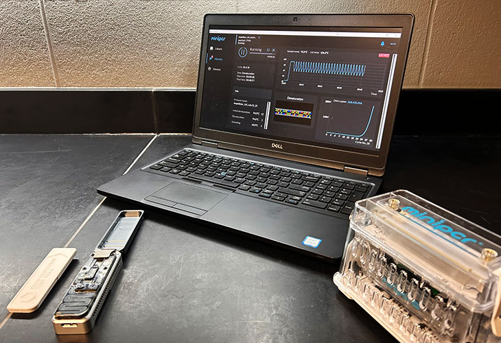 A laptop displaying a software dashboard with charts and data metrics, accompanied by an opened nanosequencer.