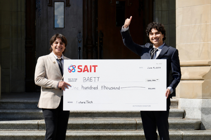 Two SAIT students stand outside holding a large cheque